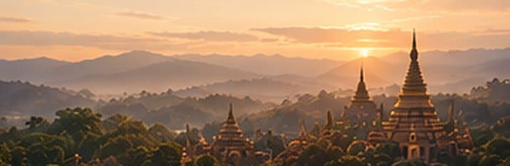 Golden pagodas rising from a forest at sunset, with hills beyond